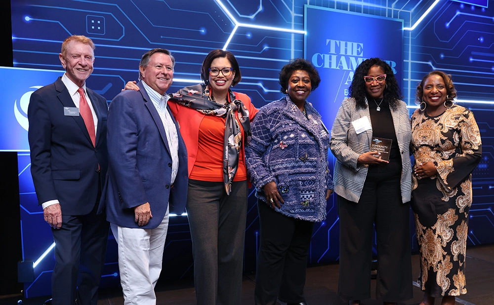 Smiling group of four Black women and two white men, all professionally dressed, in front of a sign saying The Chamber ALX: Best in Business. One woman is holding a glass award plaque.