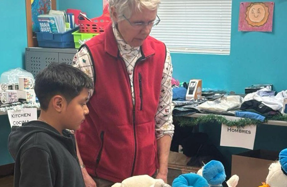 Mature caucasian woman with short white hair and glasses with a young Latino boy, looking at gifts together at the holiday gift event where children could select gifts for their families.