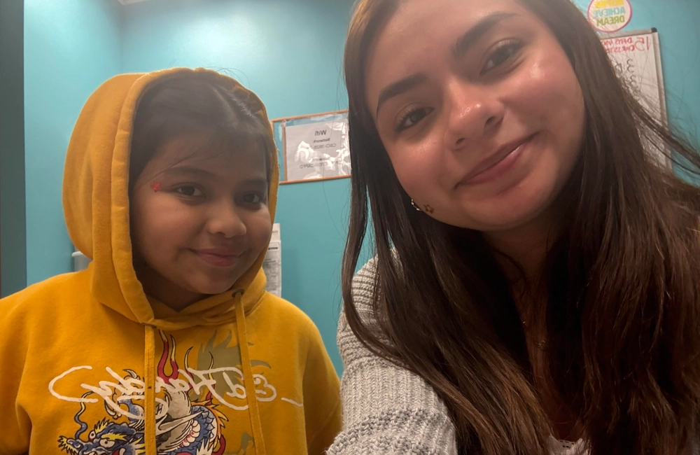Young Latina woman smiling next to a younger Latina girl