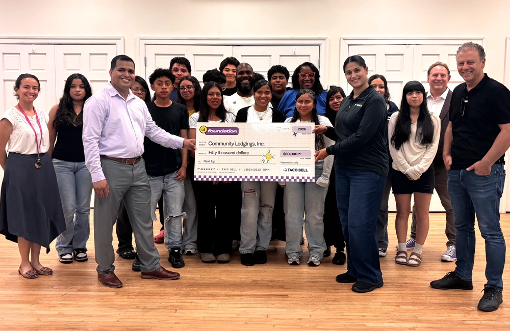 Group of mostly non-White youth and adults smiling and holding a large check for $50,000 made out to Community Lodgings.